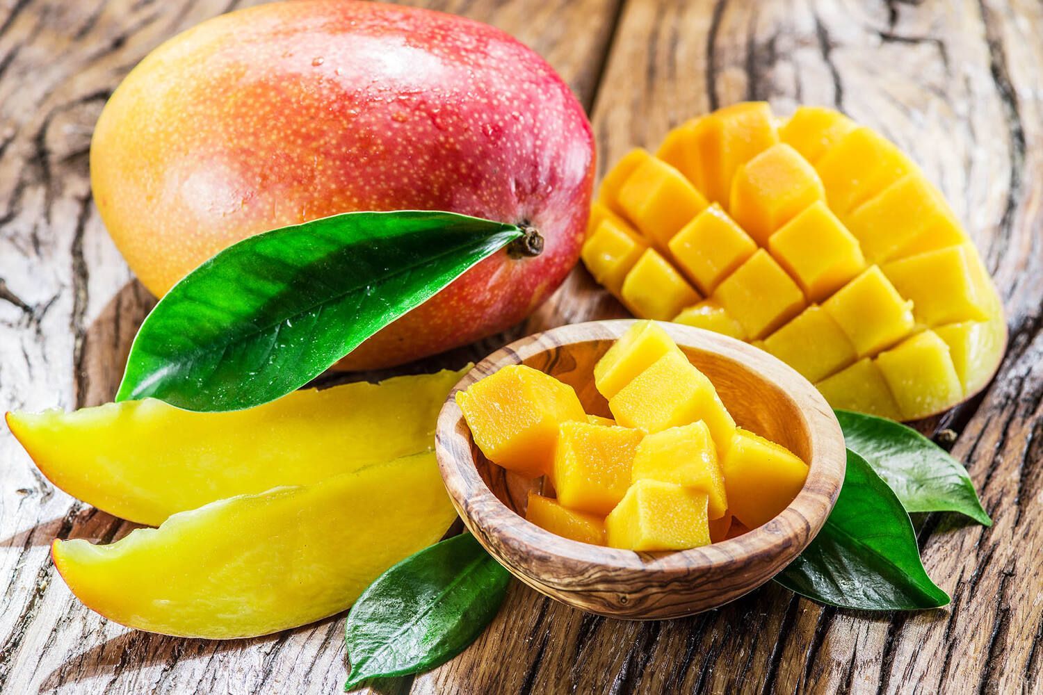 Hele en gesneden mango's met bladeren op een houten ondergrond.
