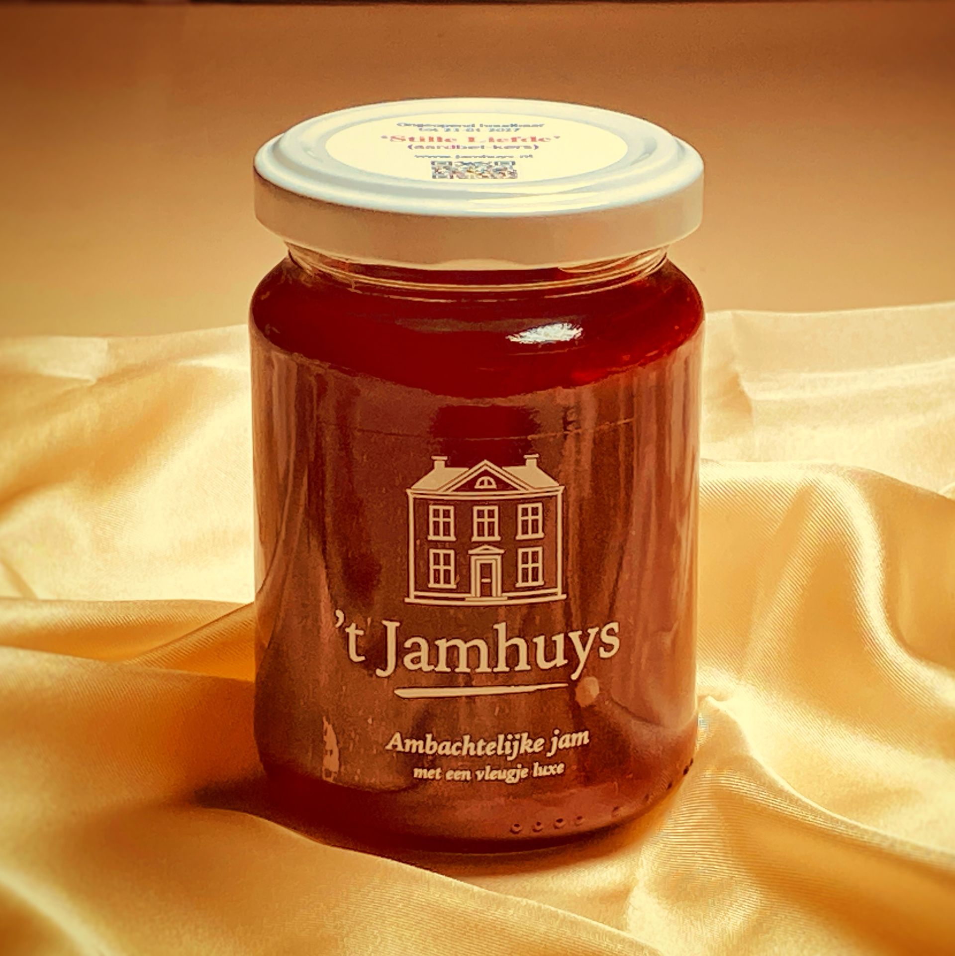 Een pot jam met een wit deksel en etiket, op een crèmekleurig zijden doek.