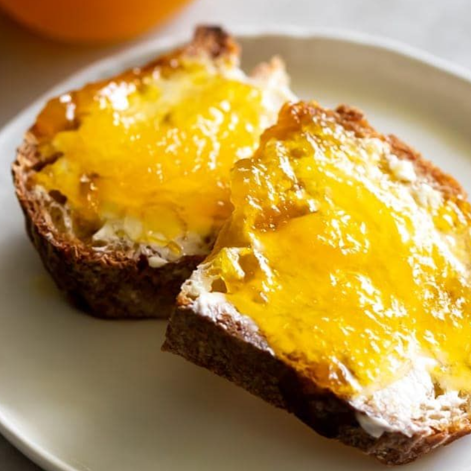 Geroosterde sneetjes brood met romige spread en sinaasappeljam op een wit bord.