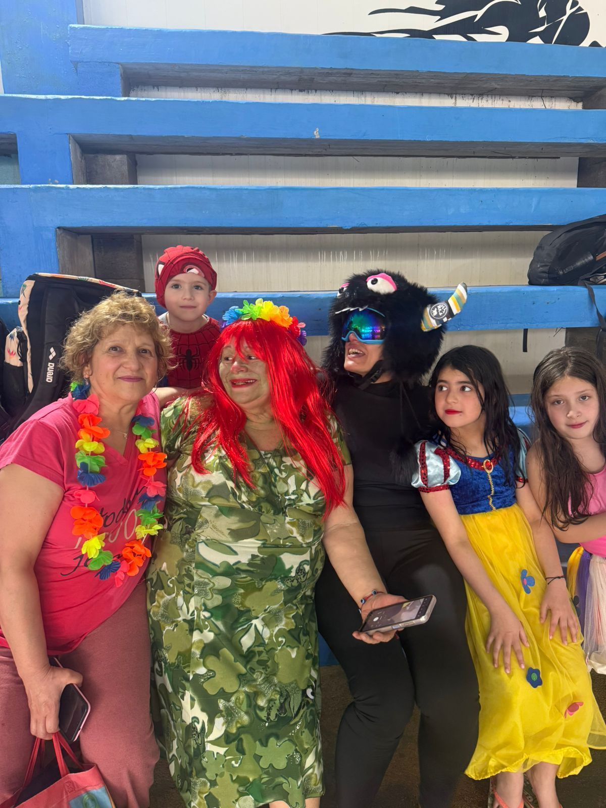 Grupo de personas disfrazadas posando en el interior, incluida una mujer con un sombrero de monstruo y una niña con un vestido de Blancanieves.