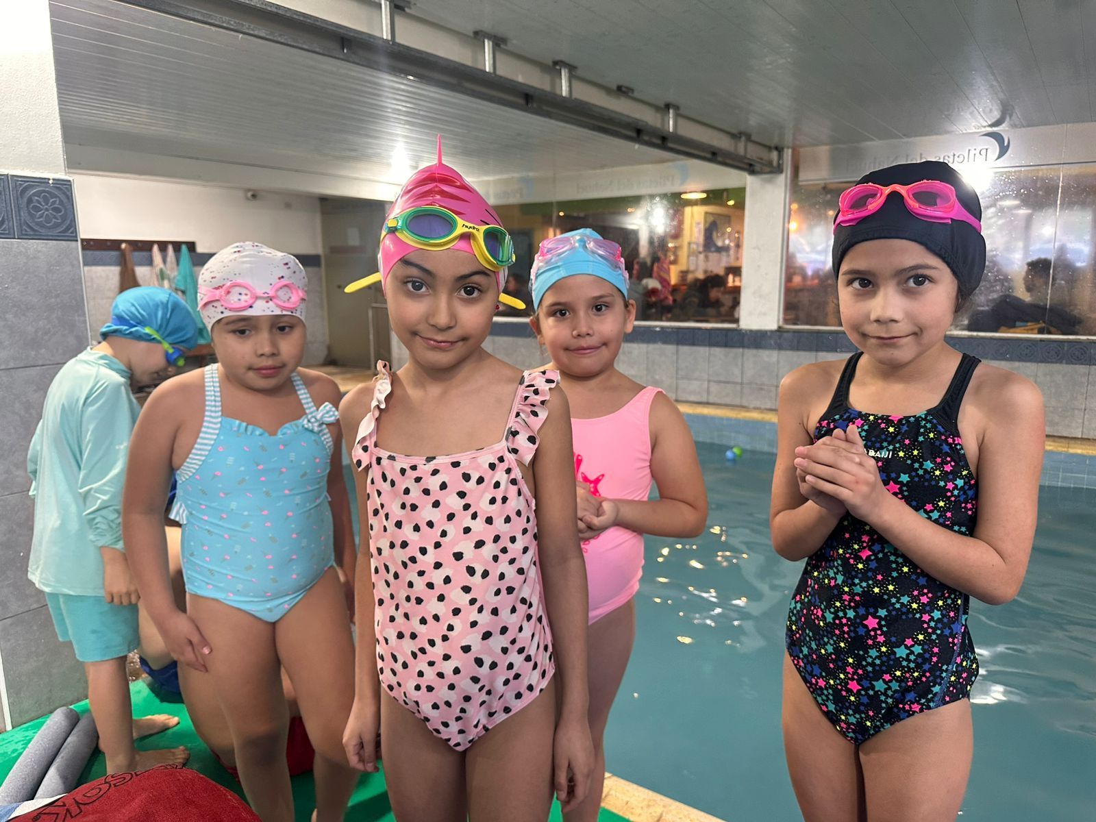 Cinco chicas jóvenes en traje de baño y gorras están cerca de una piscina.