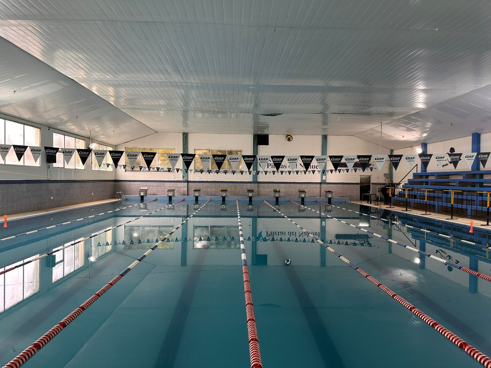 Piscina cubierta con carriles y tacos de salida y banderas en la parte superior.