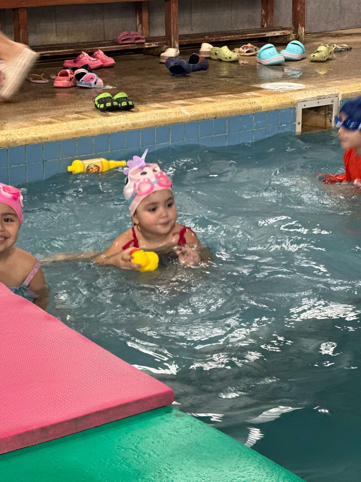 Niños con gorros de baño jugando en una piscina con juguetes.