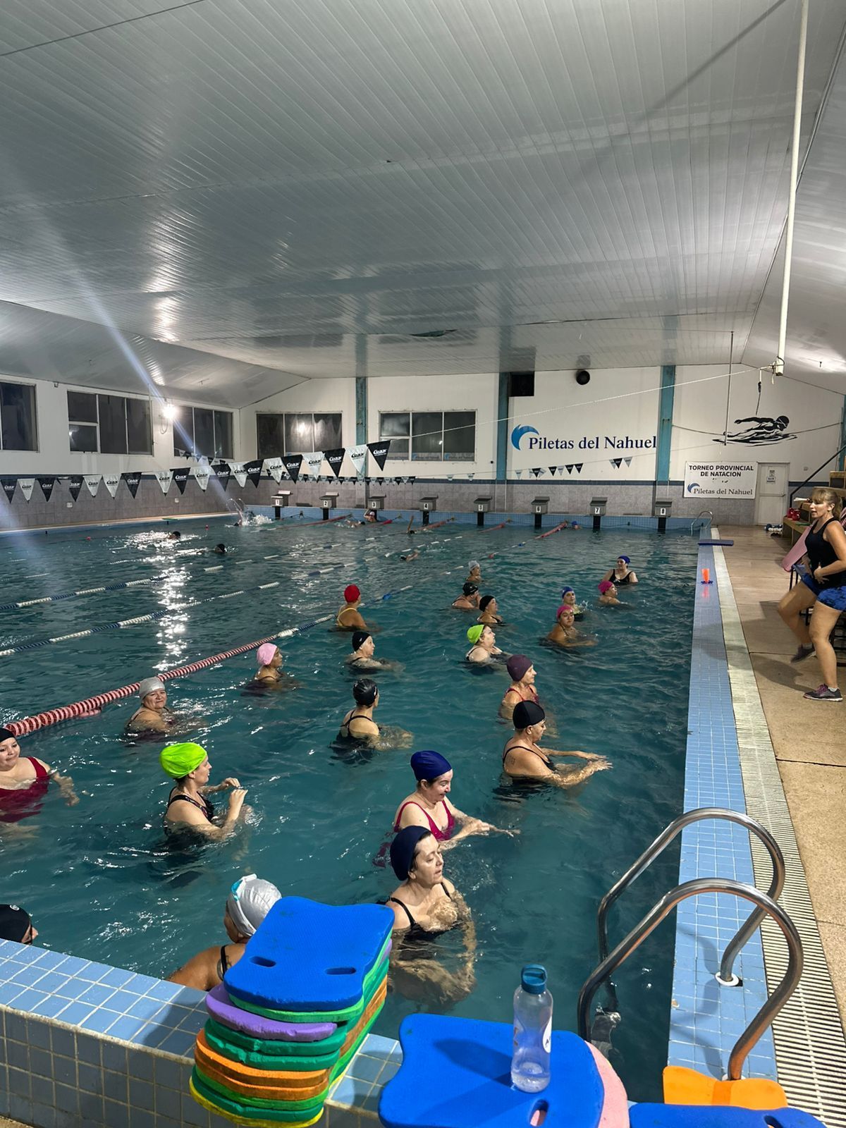 Personas en una piscina haciendo aeróbic acuático, usando gorros de baño.