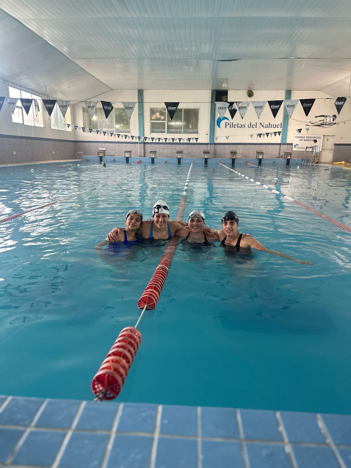 Cuatro personas sonriendo en una piscina, posando para una foto.
