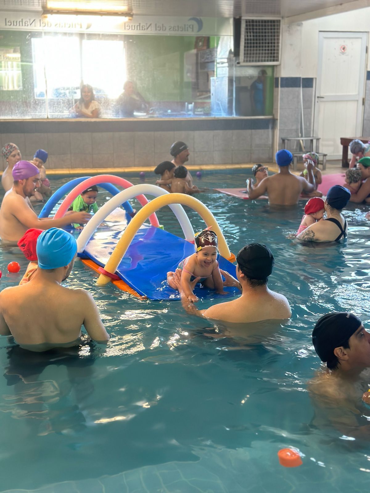 Personas con niños en una piscina. Algunos usan inflables. Otros los sostienen.