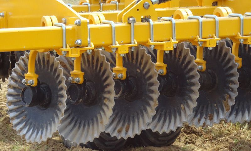A close up of a yellow and black disc tiller in a field