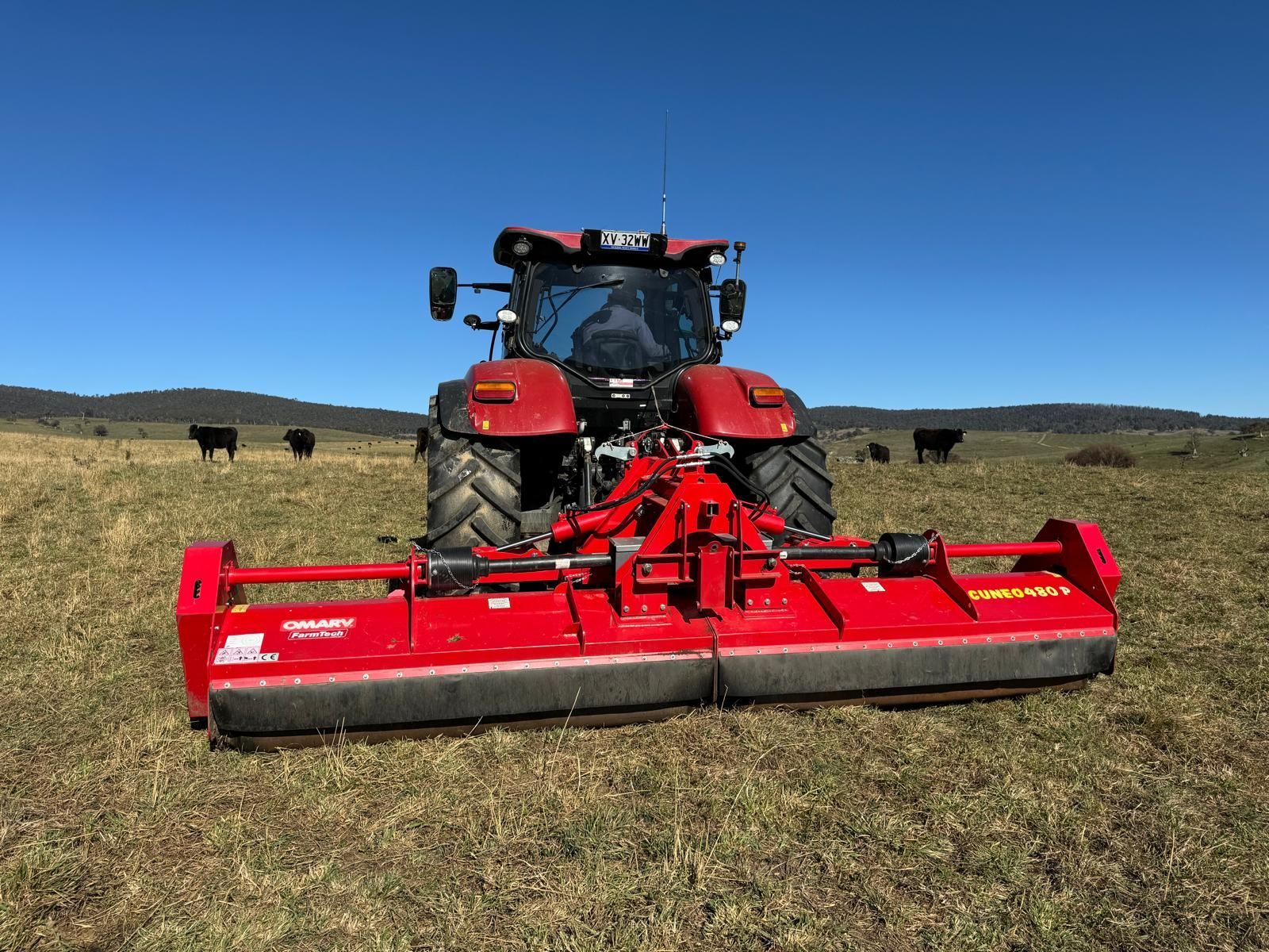 A tractor is cutting grass in a field with trees in the background