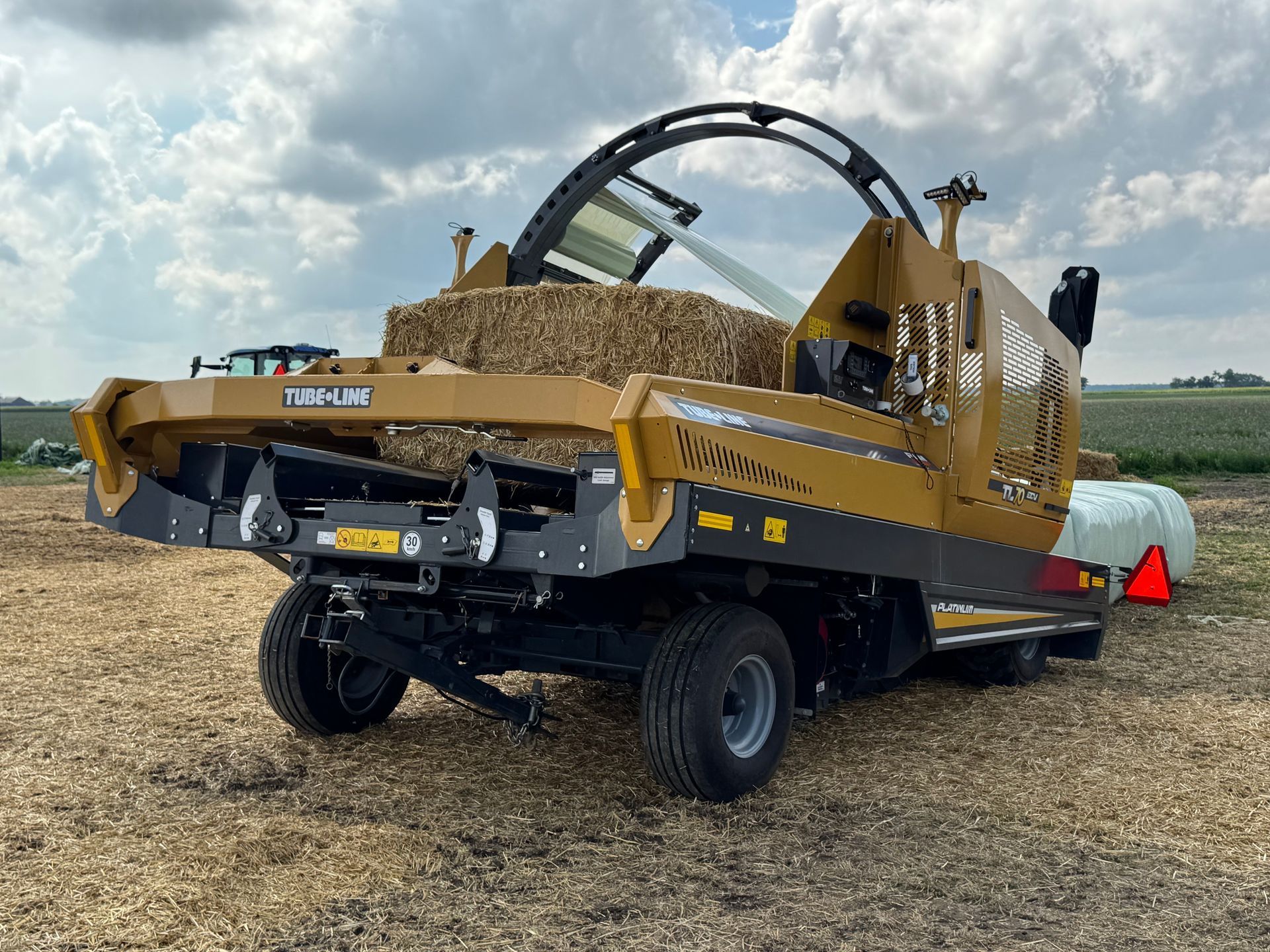 A yellow and black machine is wrapping hay bales in a field.