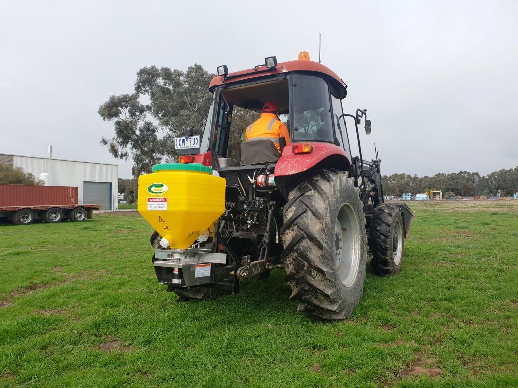 A red tractor with a fertiliser spreader is parked in a grassy field.