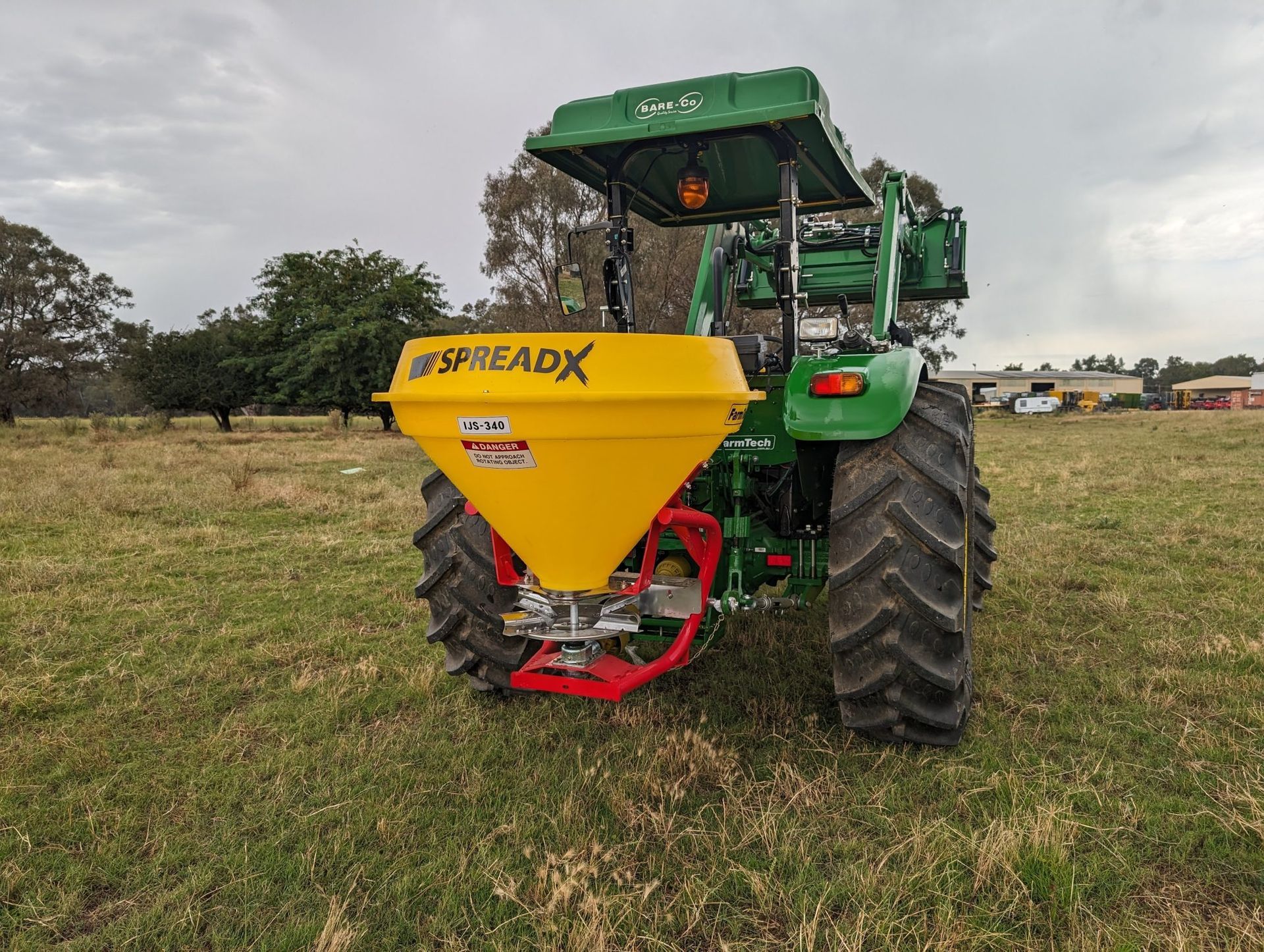 A green tractor with a yellow spreader attached to it is sitting in a grassy field.