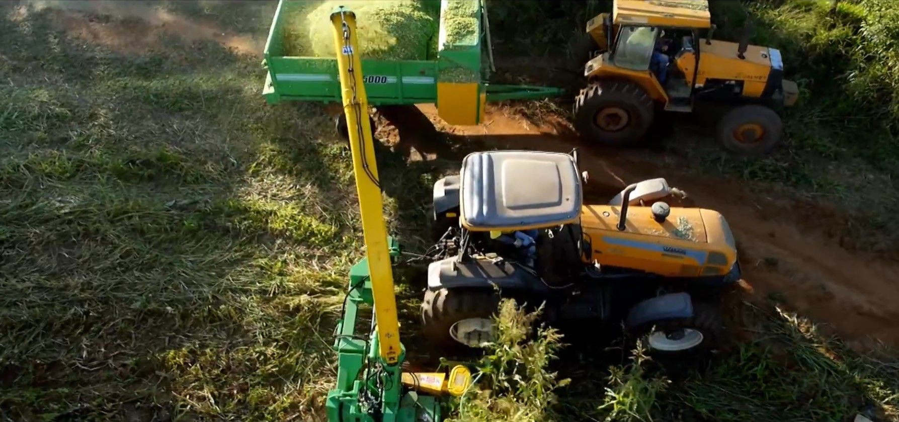 A blue tractor is cutting grass in a field.