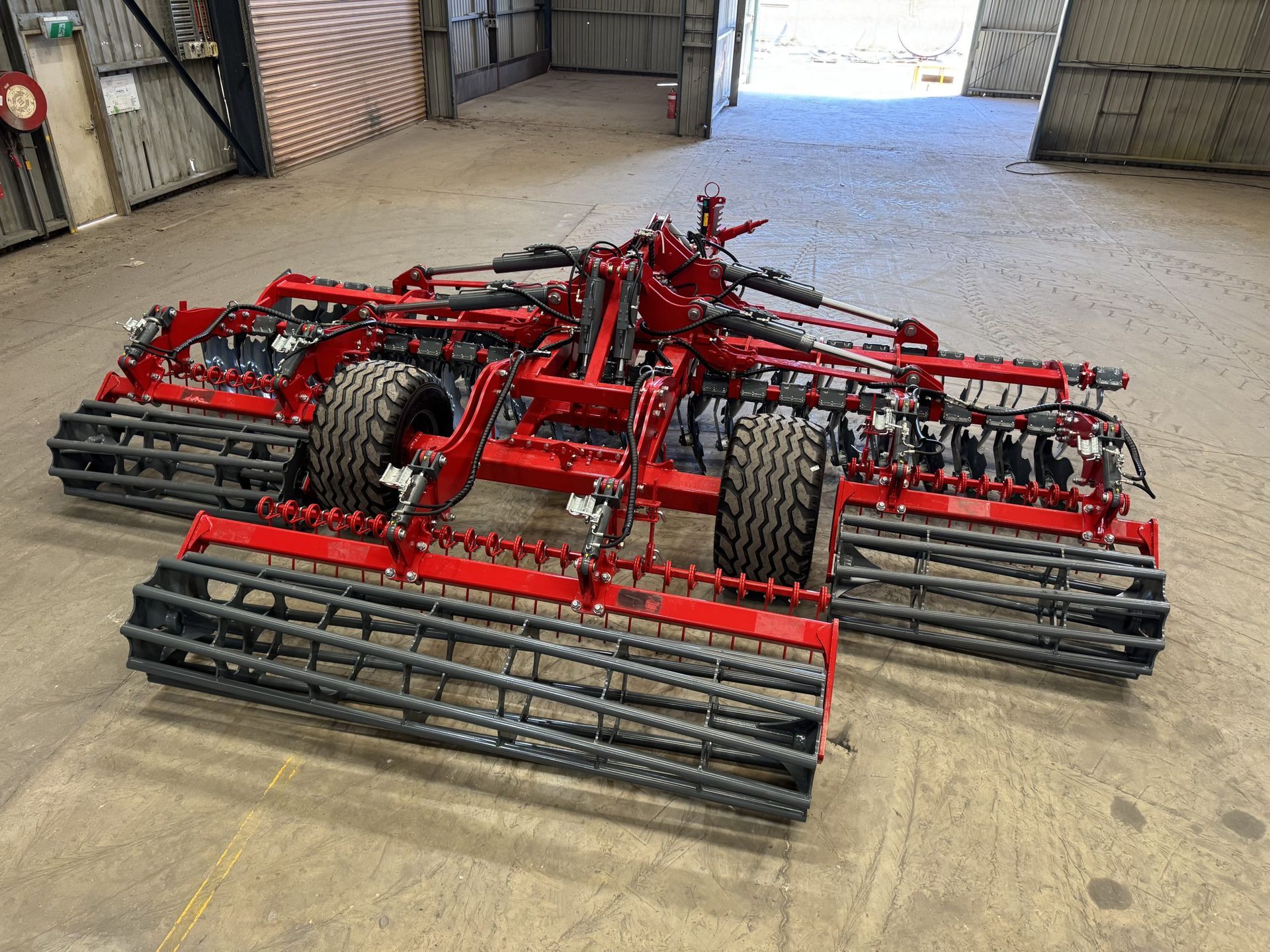 A red and gray disc tiller is parked in a grassy field.
