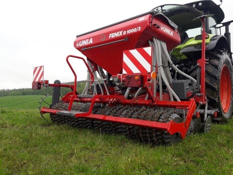 A red and white seed drill is parked in a grassy field.