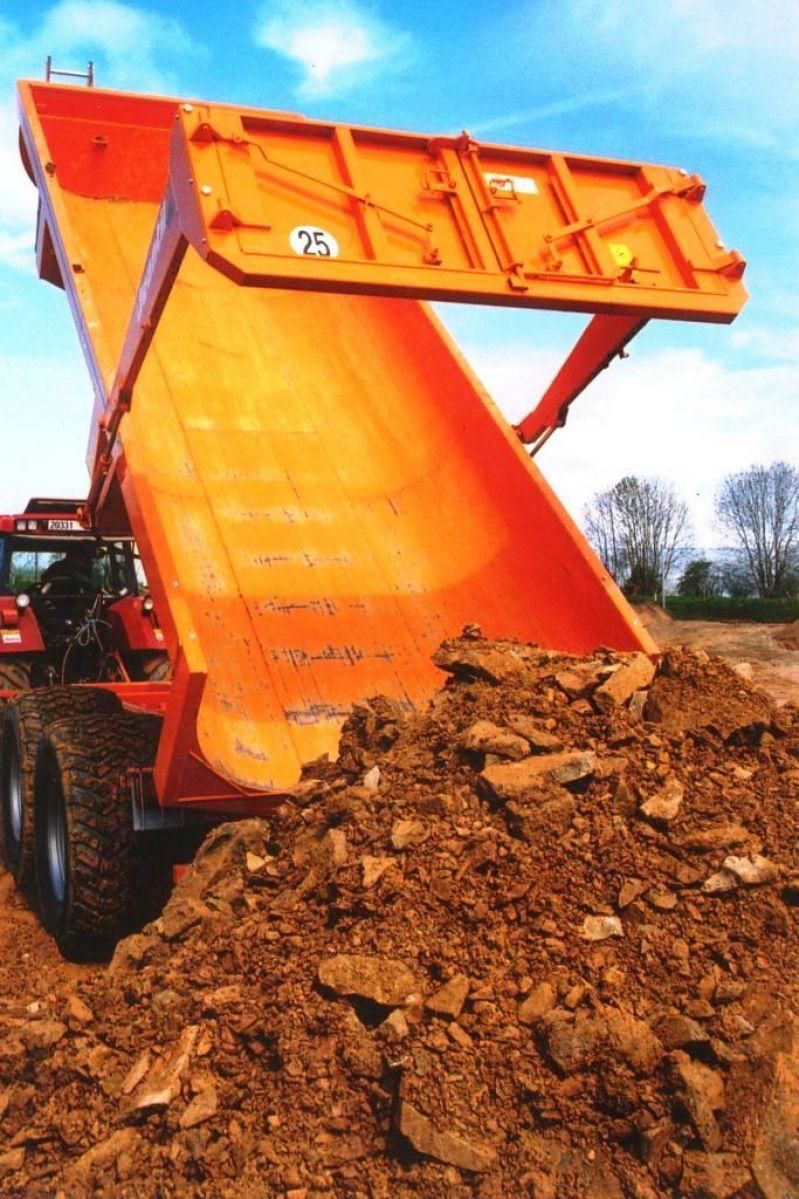 A yellow trailer is attached to a tractor in a dirt field.