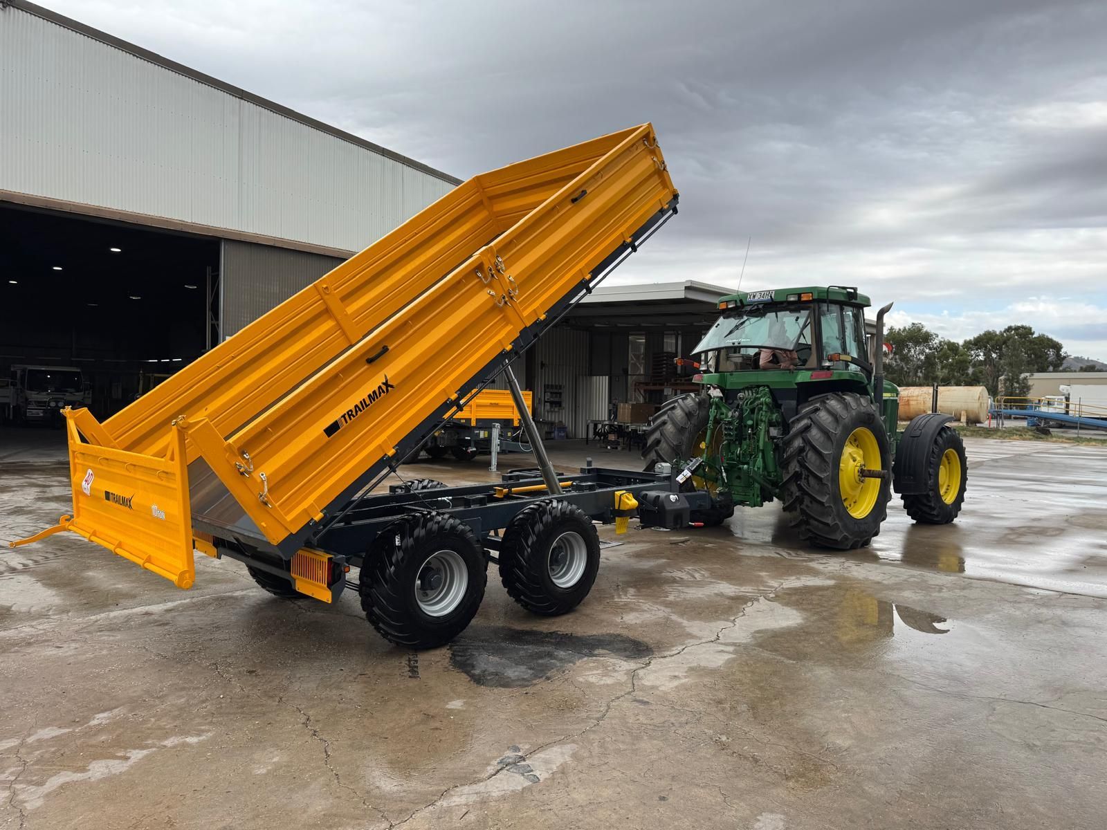 A yellow dump truck is parked next to a tractor in a dirt field.