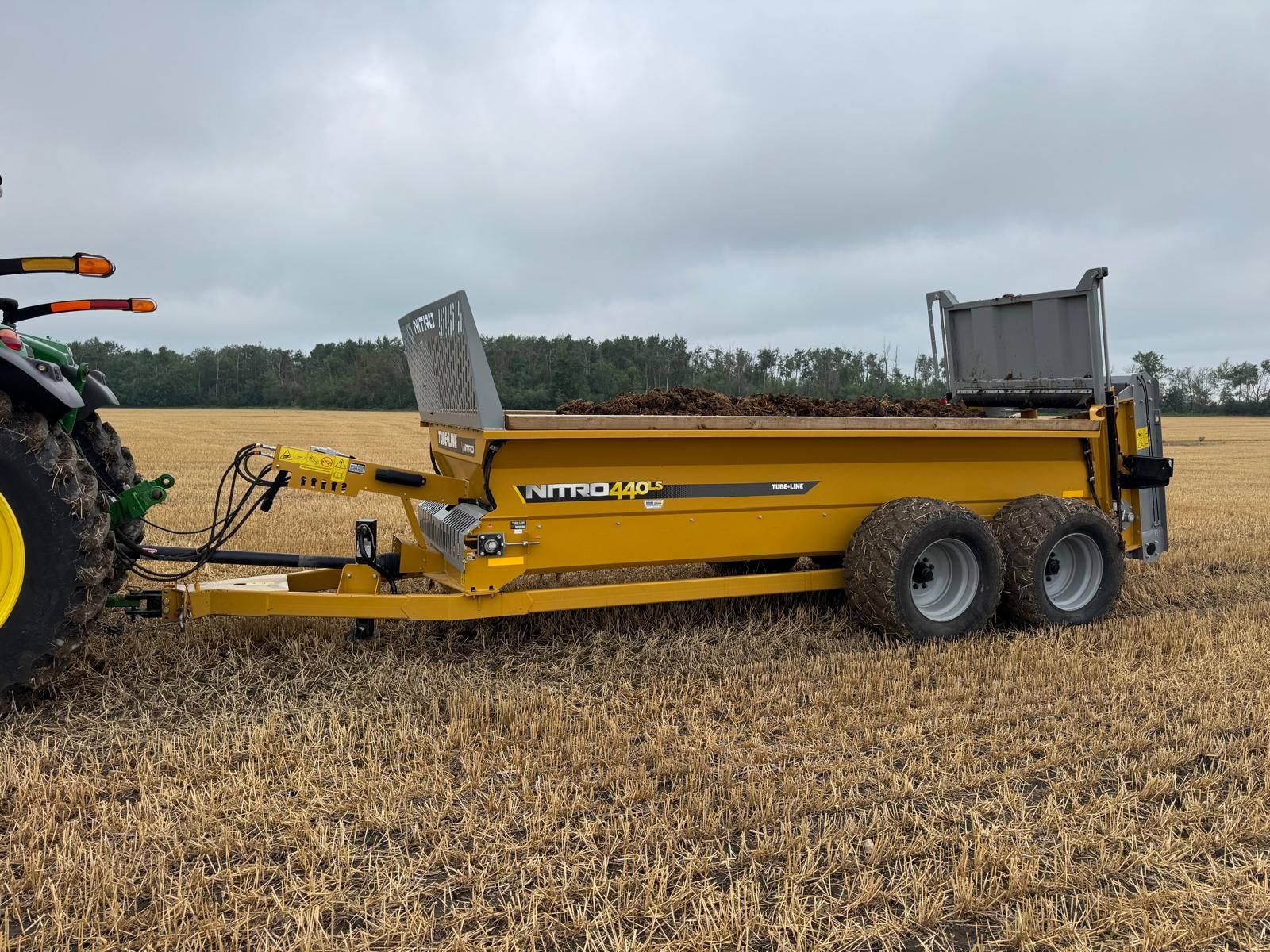 A green tractor is pulling a yellow trailer in a grassy field.
