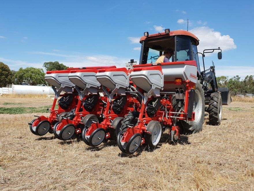 A man is driving a red and white tractor in a field with a pneumatic precision planter attached