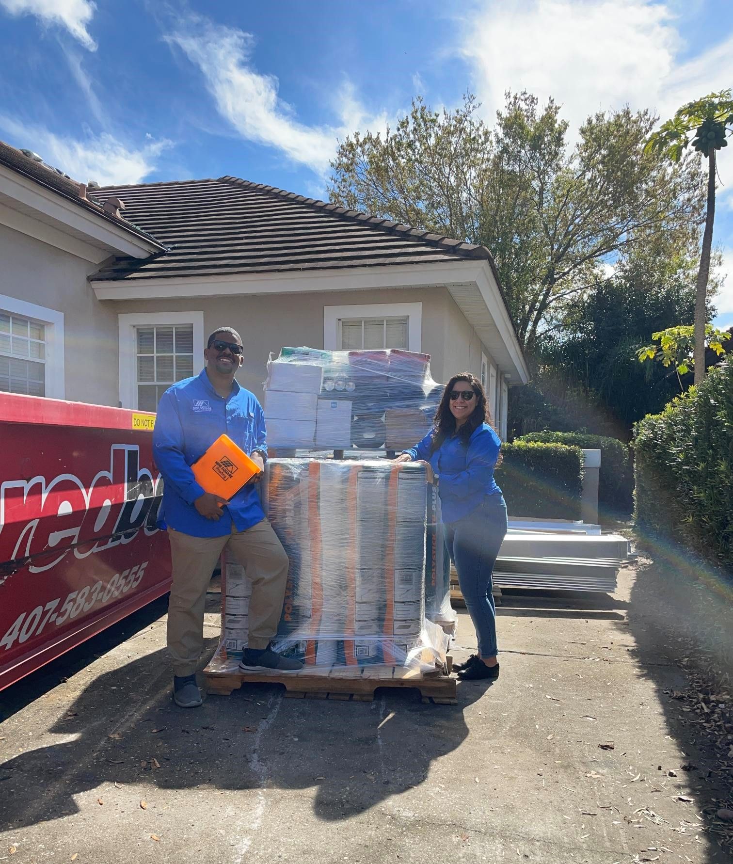 A man and a woman are standing next to a pallet of boxes in front of a house.