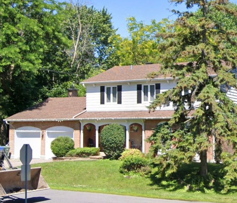 A white house with a brown roof is surrounded by trees