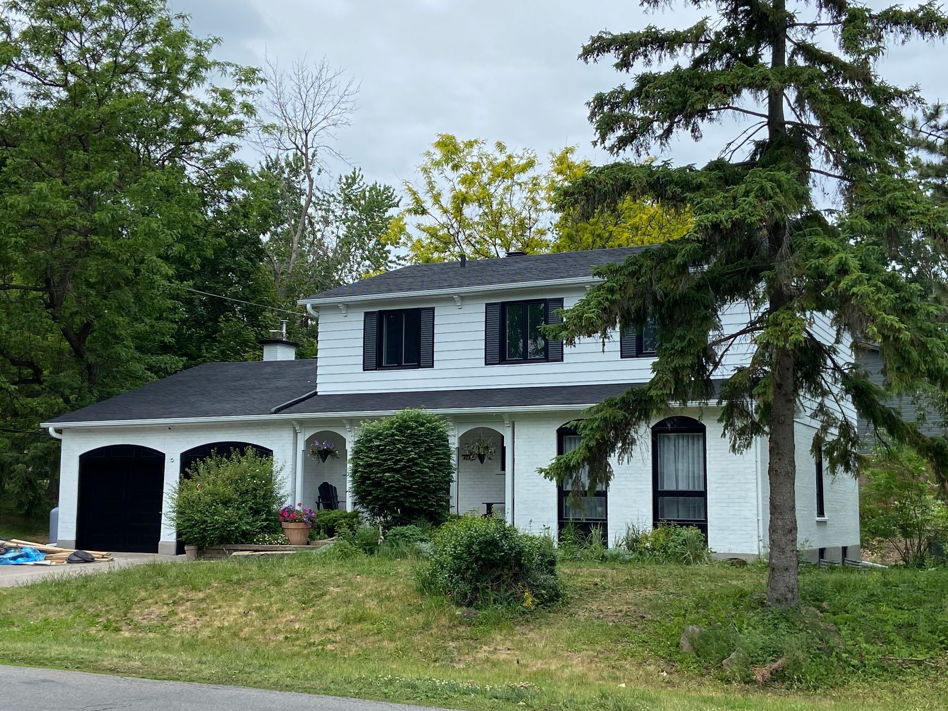 A white house with a black roof is surrounded by trees.