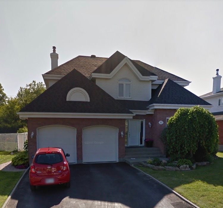 A red car is parked in front of a large house