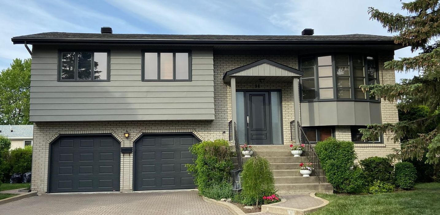A large brick house with two black garage doors and stairs leading up to it.