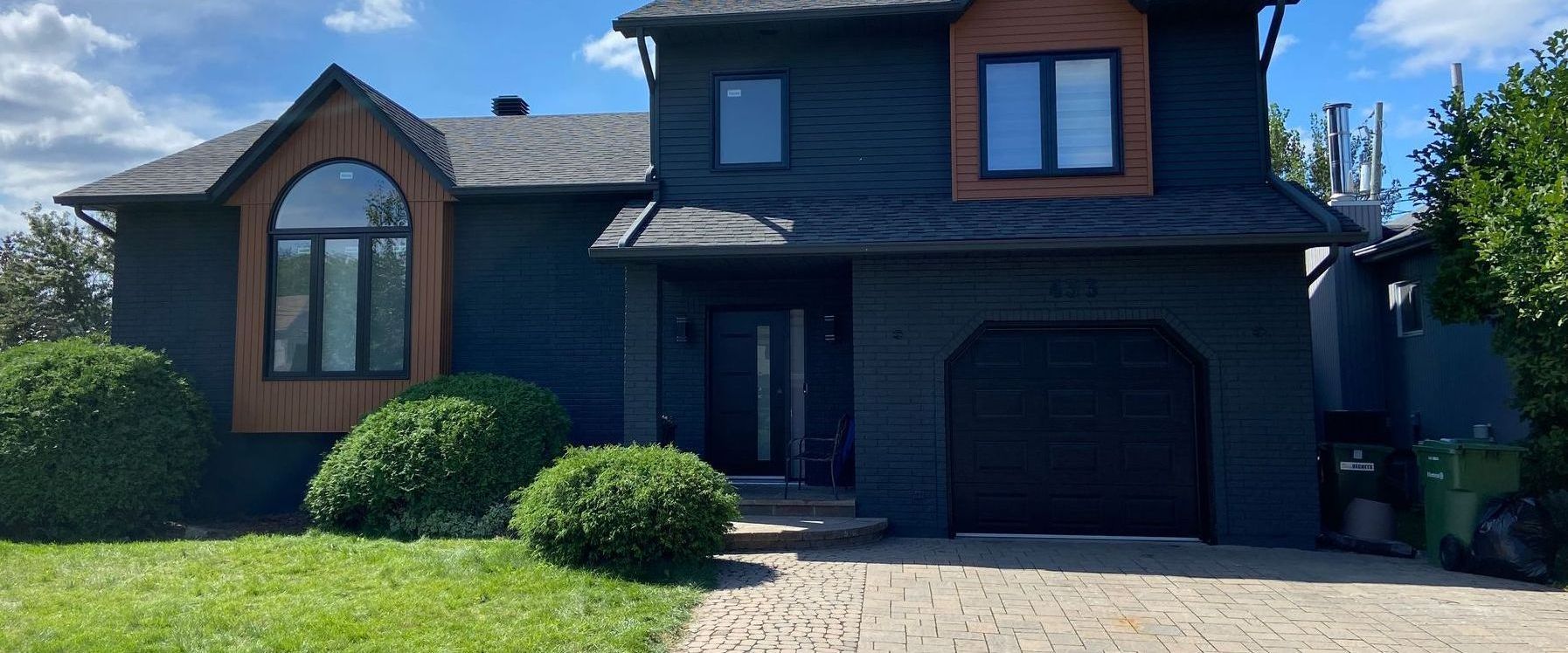 A black house with a garage and a driveway in front of it.