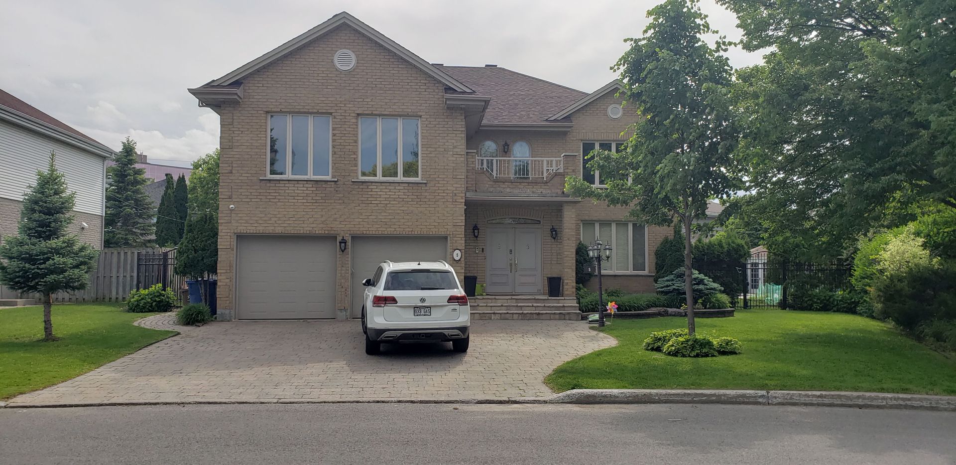 A white car is parked in front of a large brick house.