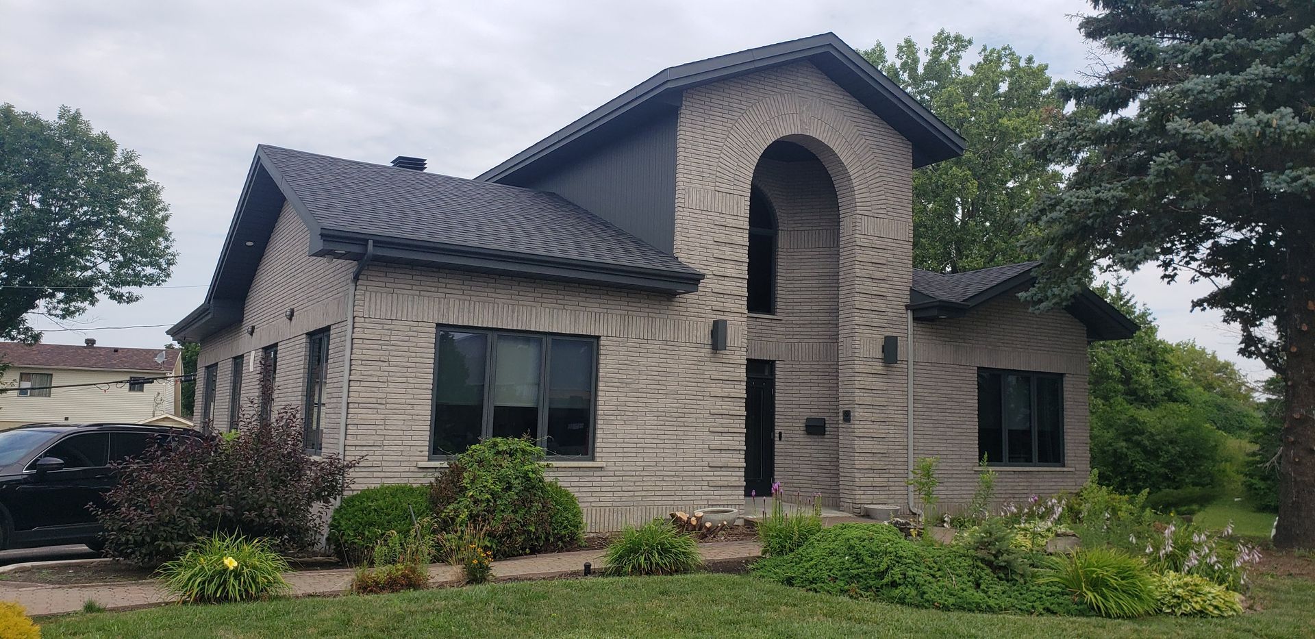 A large brick house with a black roof and a car parked in front of it.