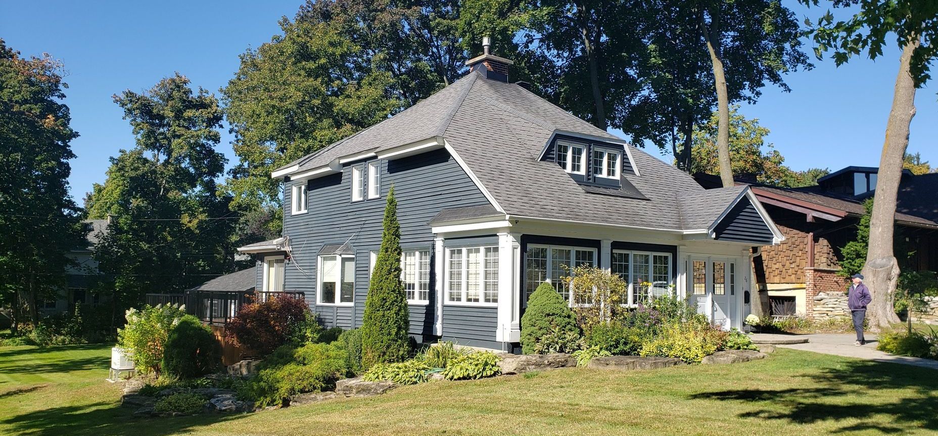 A large house with a gray roof is surrounded by trees on a sunny day.