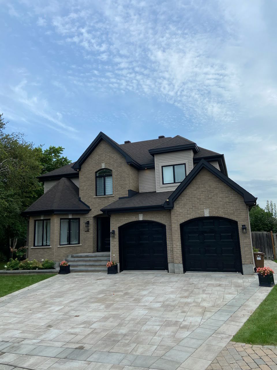 Une grande maison en brique avec deux portes de garage noires et une allée.