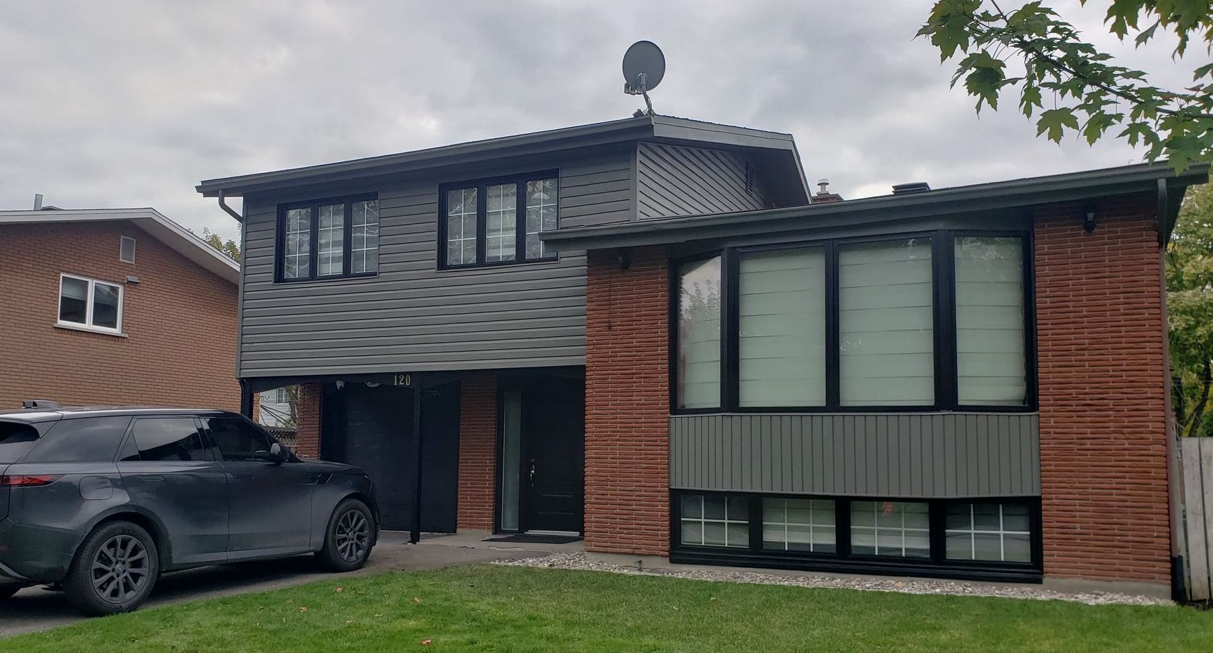 A black car is parked in front of a brick house.