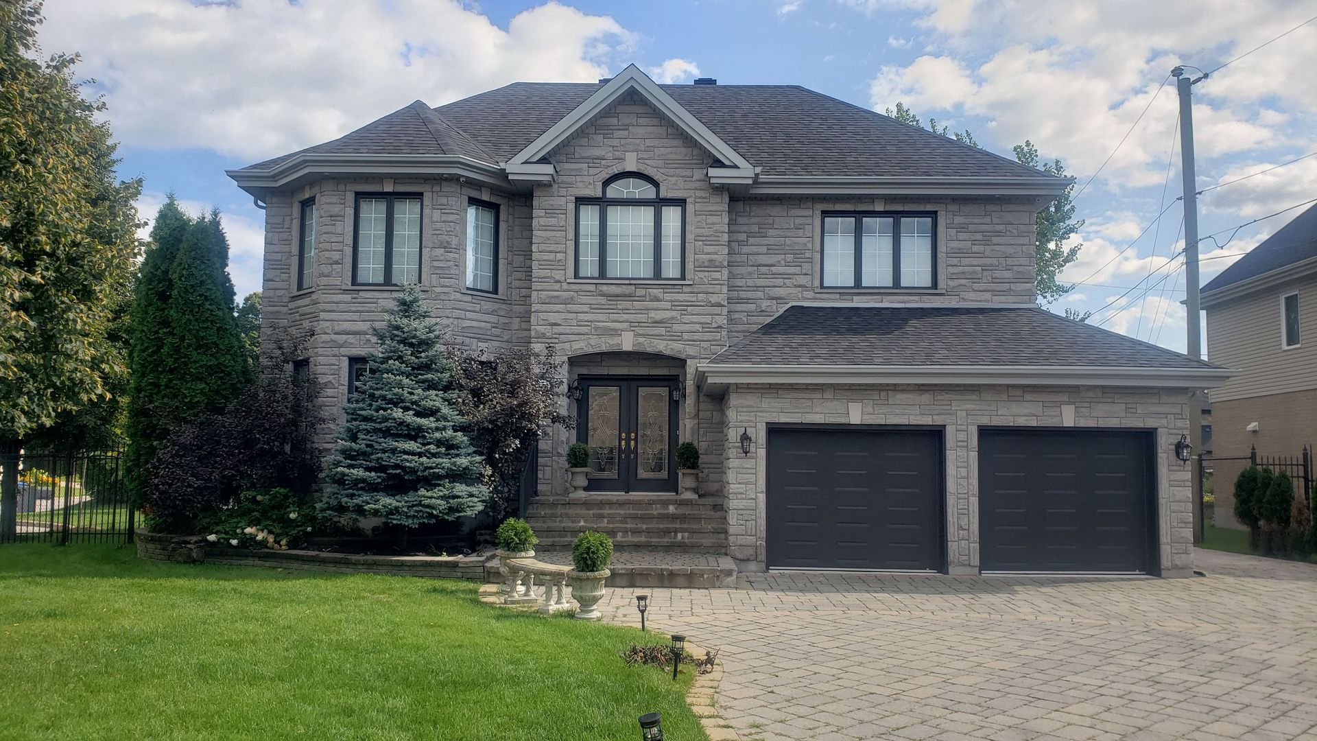A large brick house with two garages is sitting on top of a lush green lawn.
