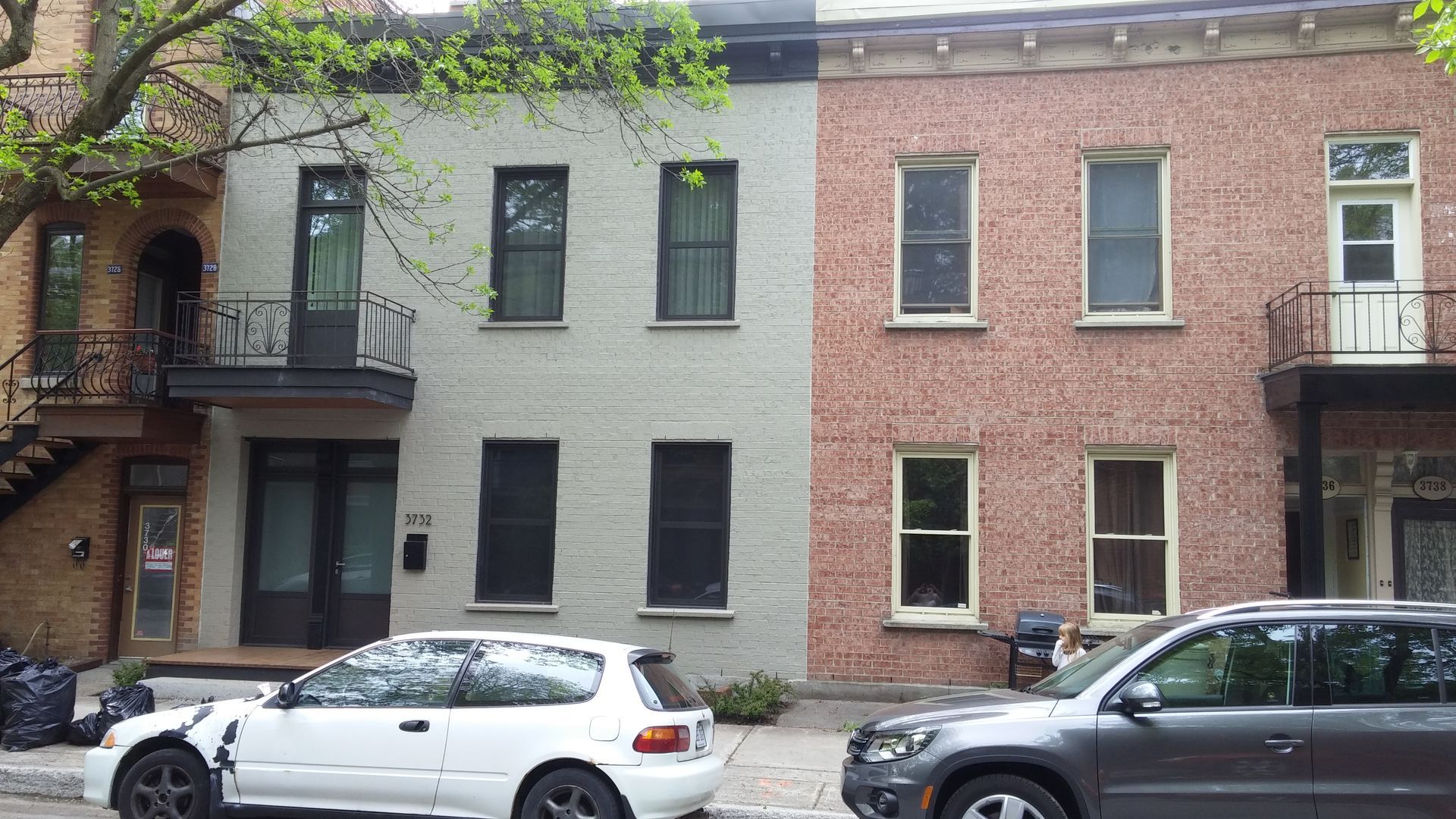 A white car is parked in front of a brick building