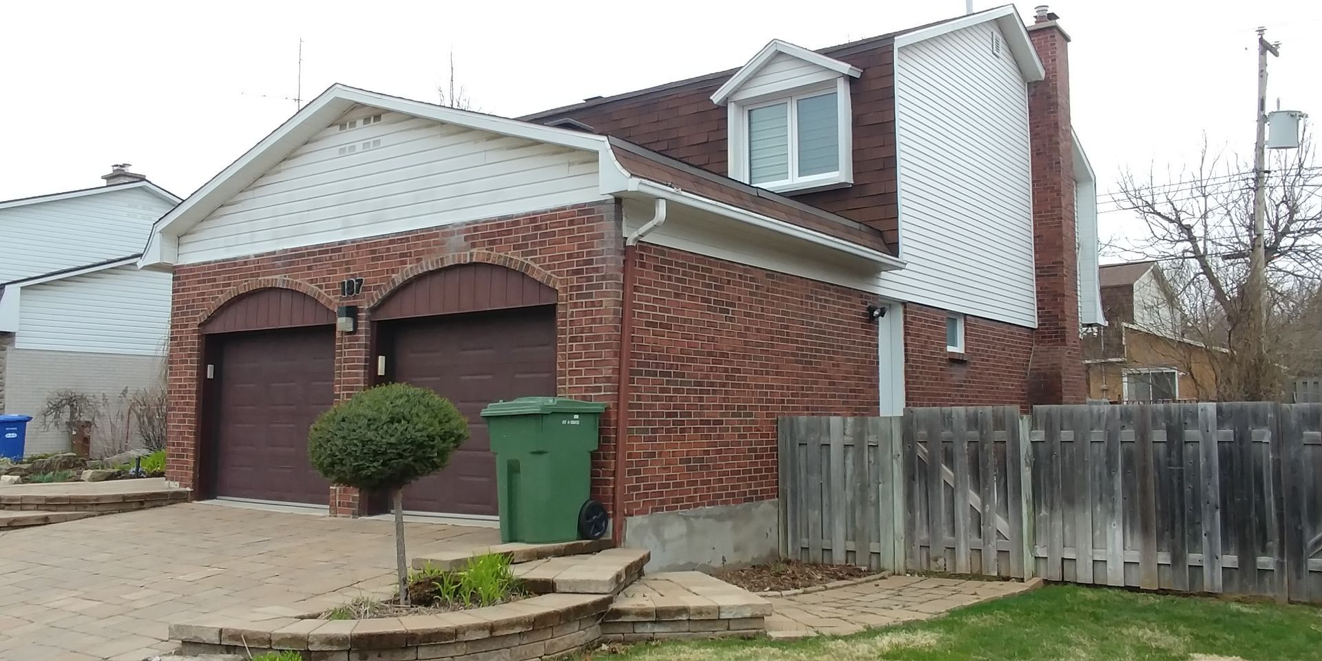 A brick house with a green trash can in front of it