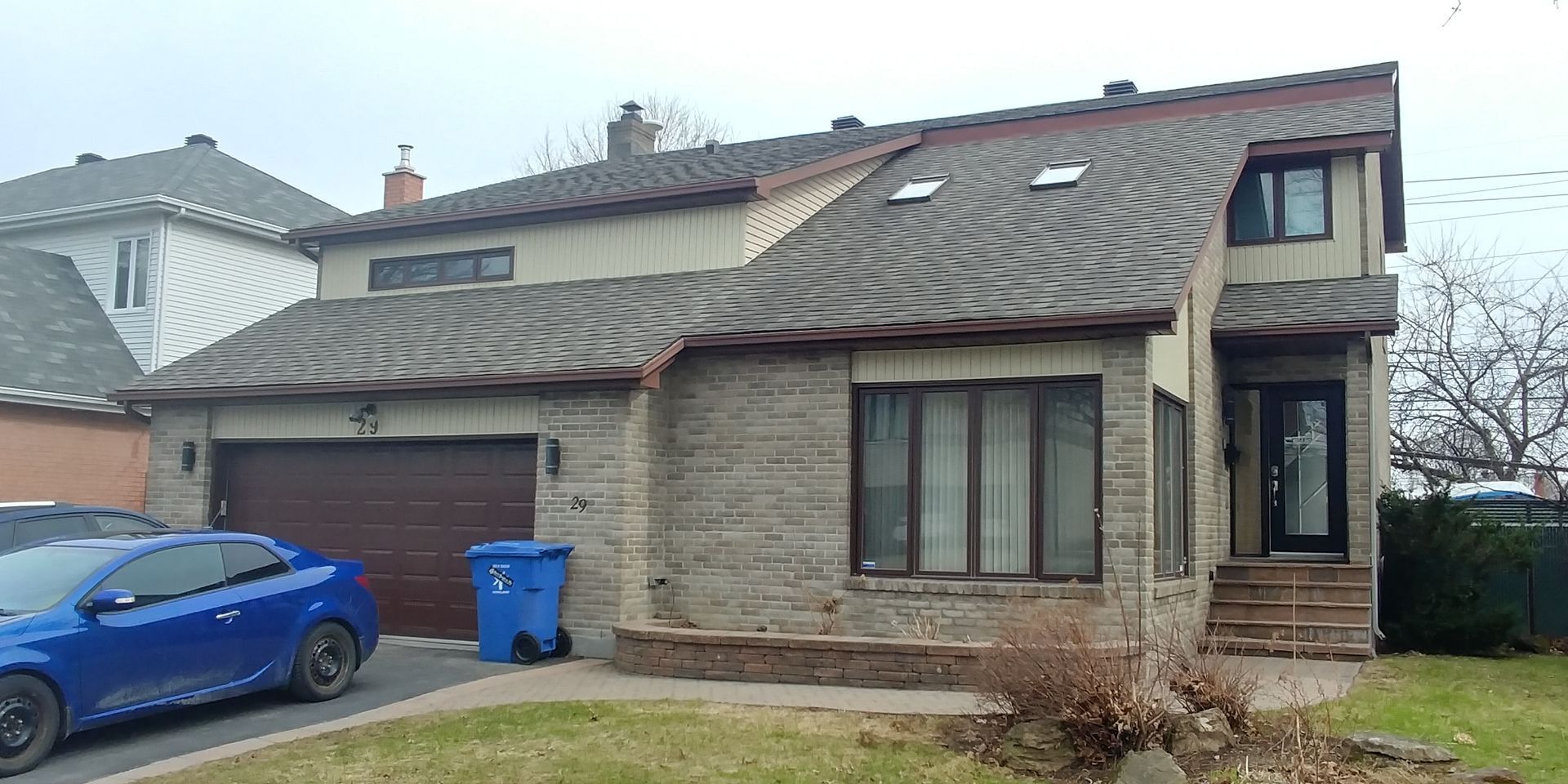 A blue car is parked in front of a brick house.