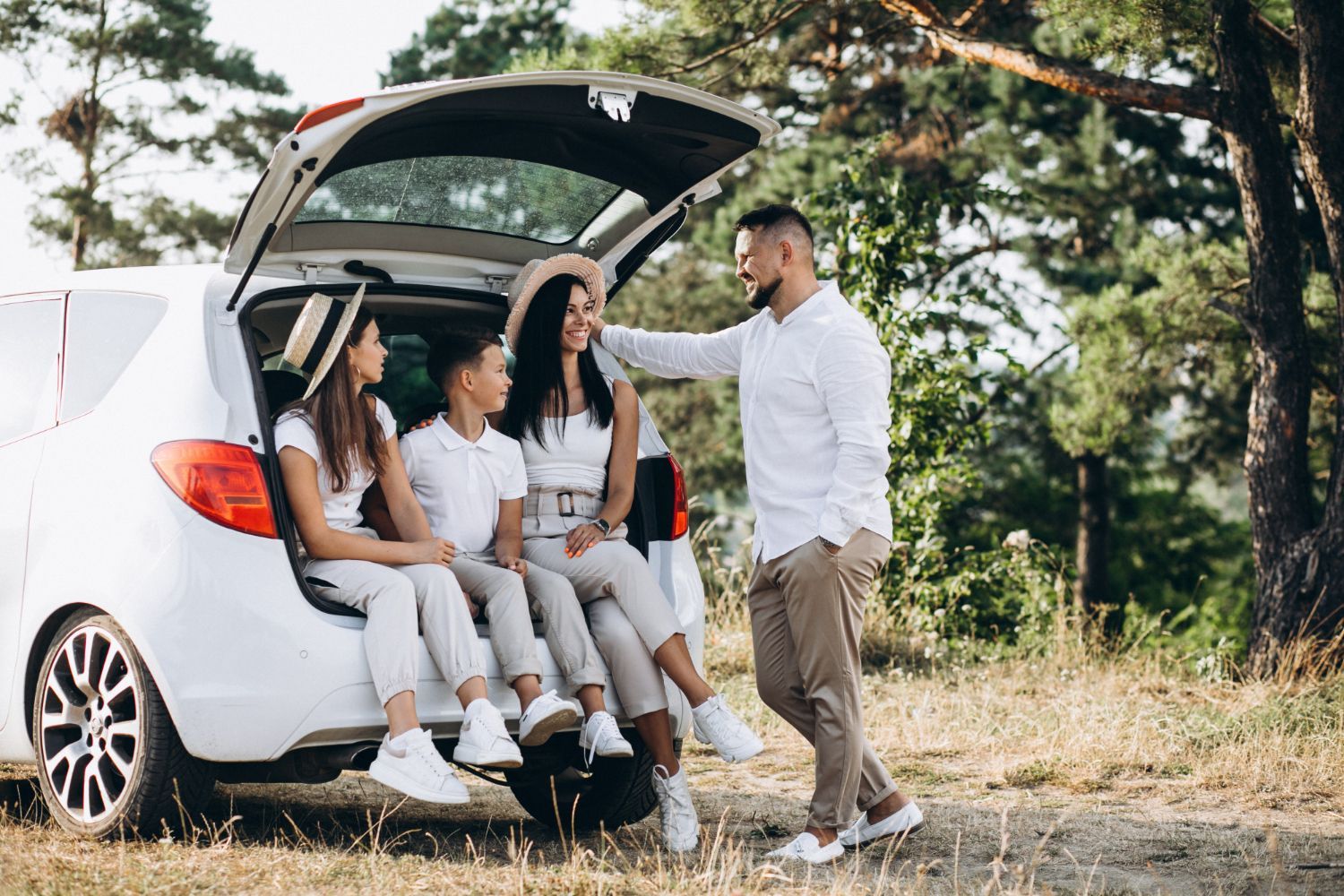 Friends seated in an open white SUV trunk talking outdoors by trees