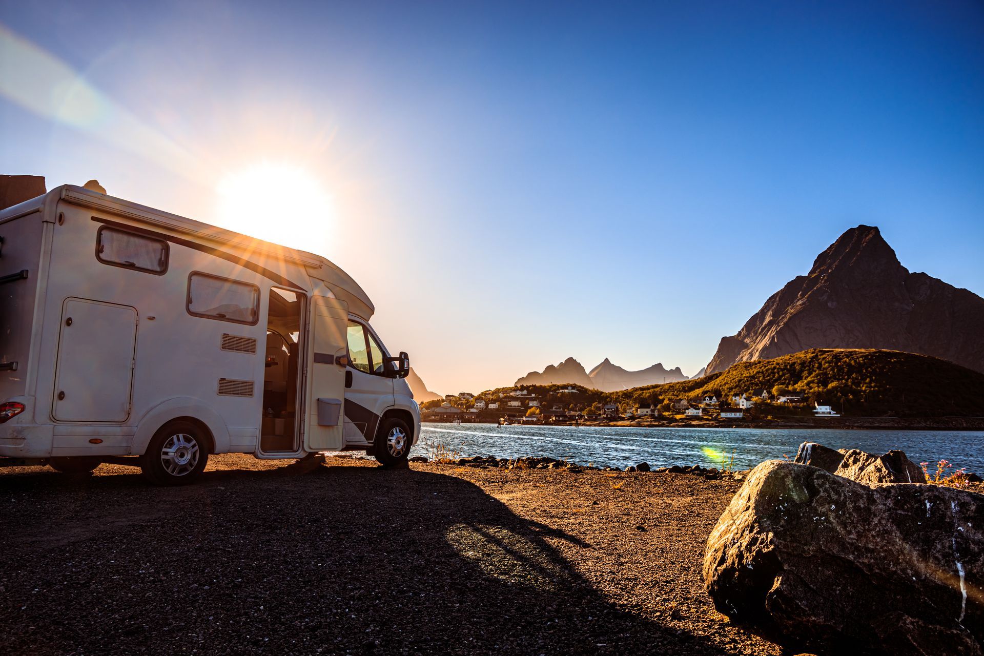 Camper van parked by a rocky shore at sunrise, with mountains and blue water in the background.