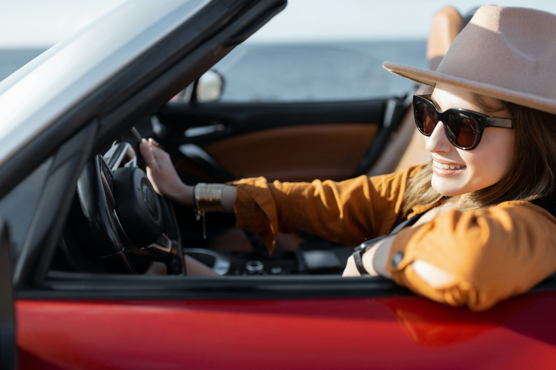 Woman in sunglasses and hat driving a red convertible on a sunny day