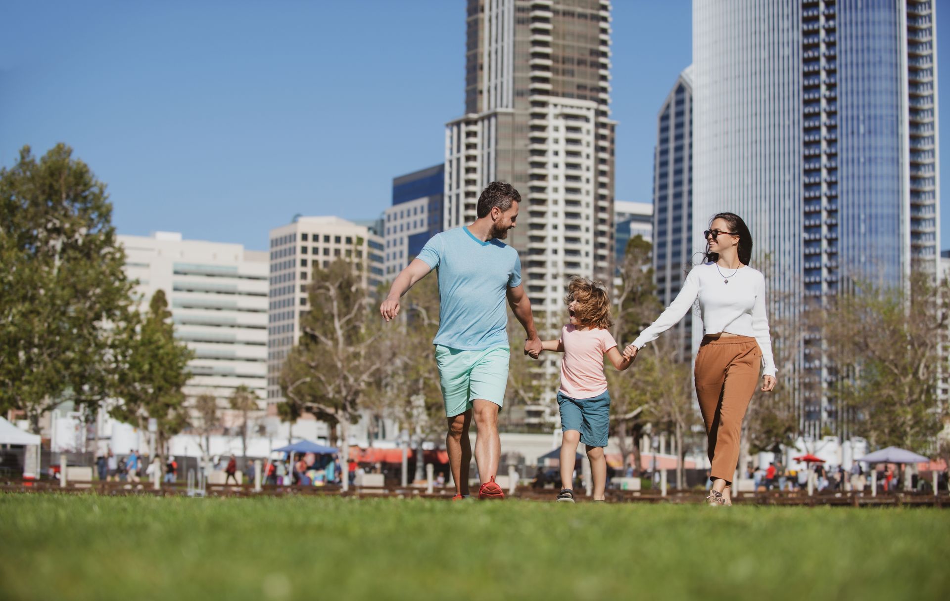 Family running on grass in a city park with tall skyscrapers in the background