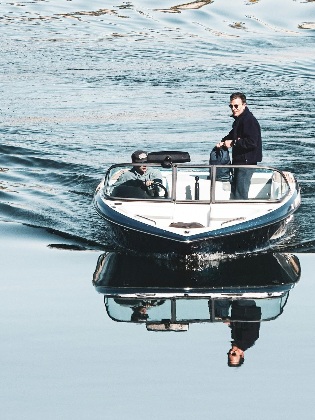 Two people on a small motorboat on calm water, with reflections visible below.