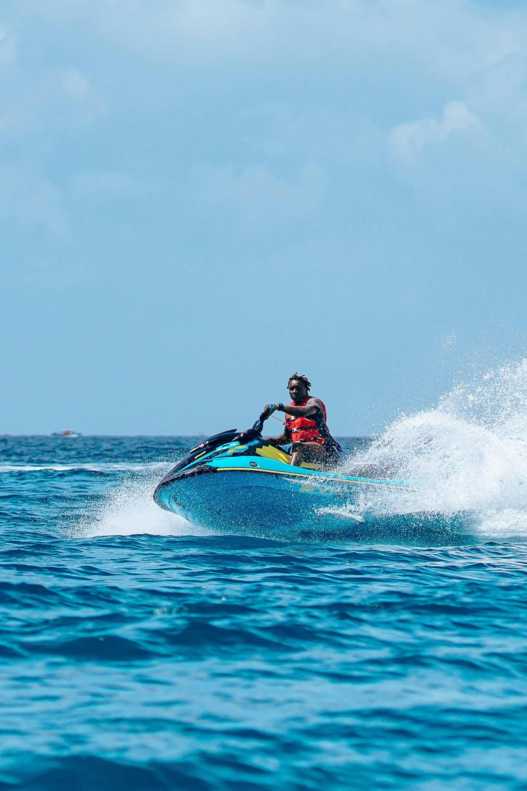 Person riding a jet ski on bright blue water, spraying waves under a clear sky