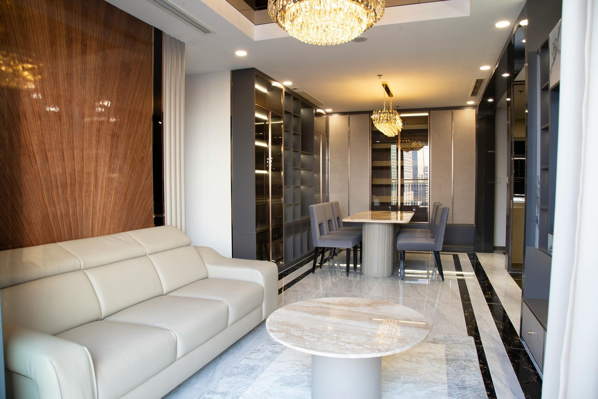 Modern living-dining room with cream sofa, marble table, chandelier, and glossy black accents
