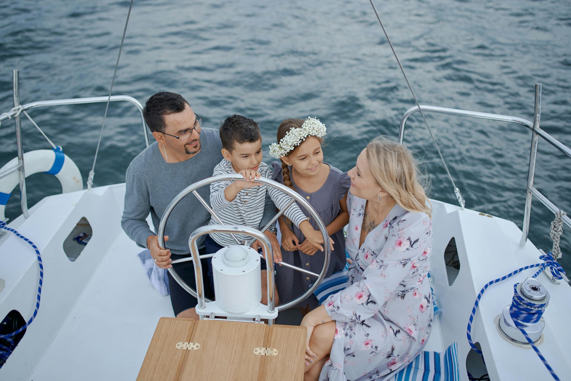 Family sitting together on a sailboat, smiling and steering on calm water