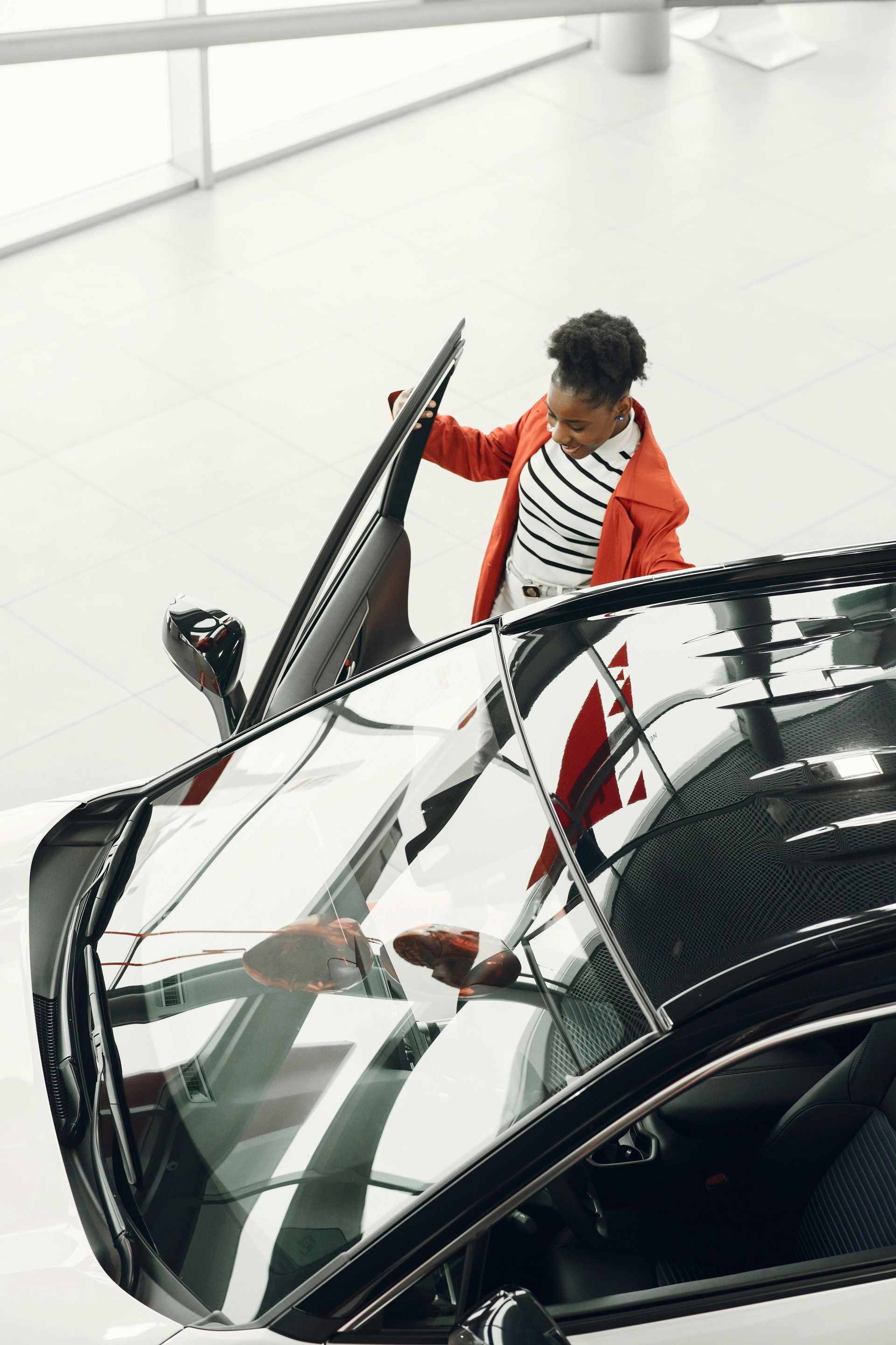 Person in an orange jacket opening the door of a black convertible in a bright showroom