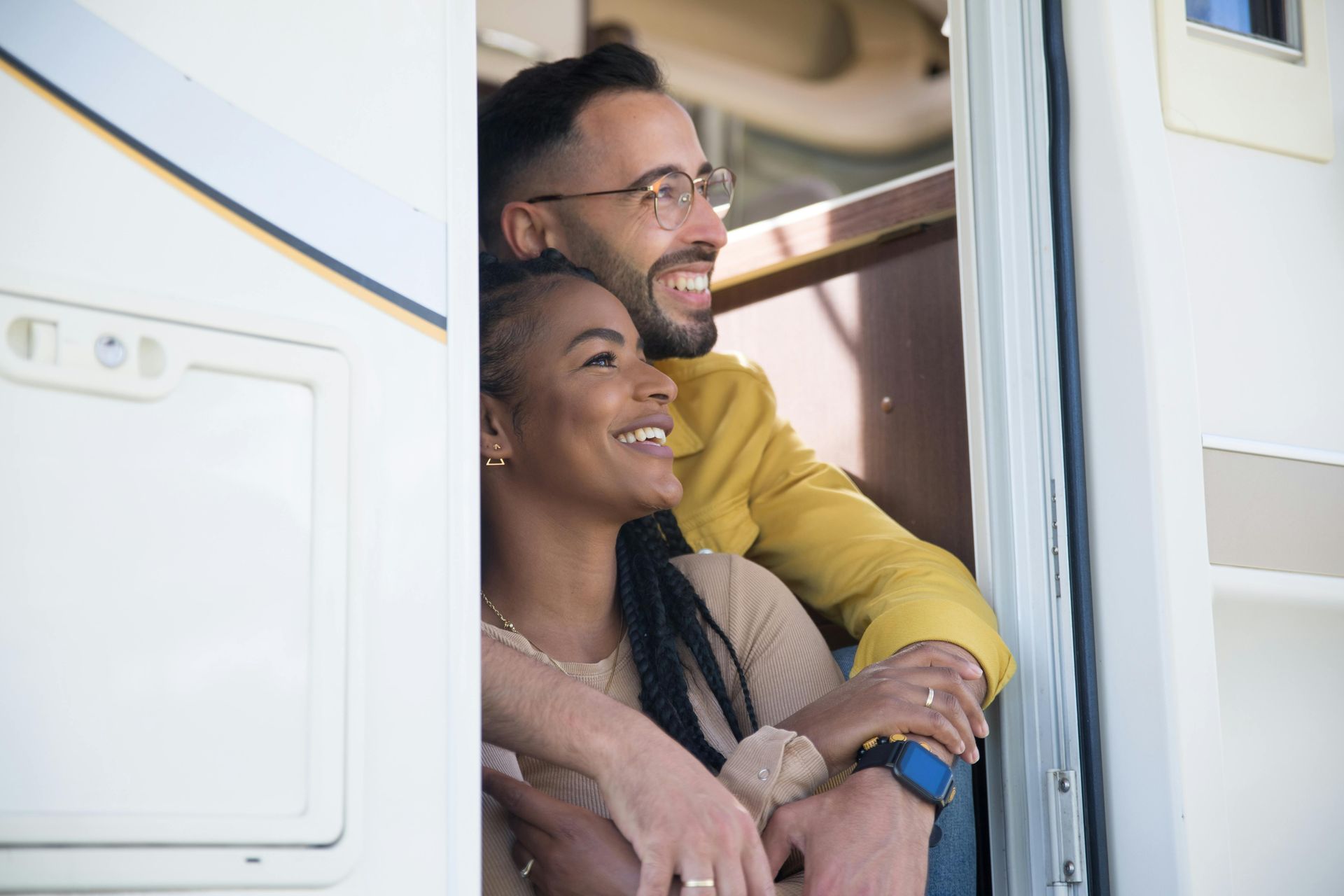 Two smiling people leaning in a doorway of an RV, looking outside