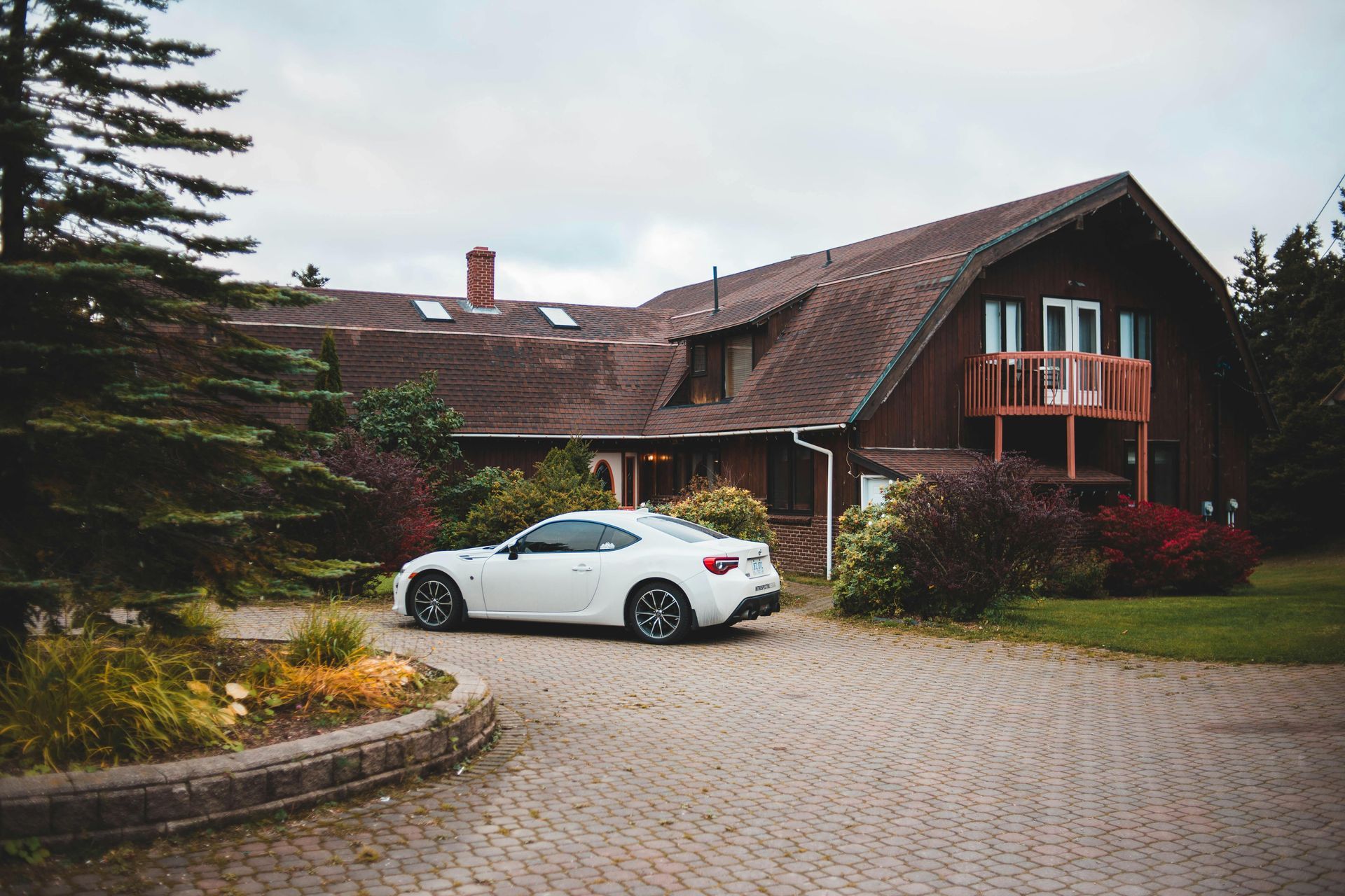 White coupe parked in front of a rustic brown lodge with a cobblestone driveway and trees
