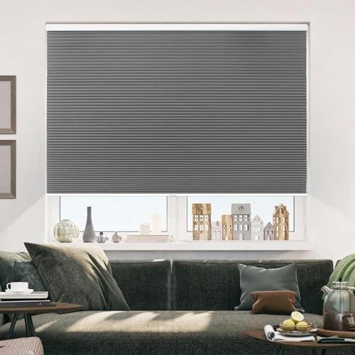 A gray honeycomb blind covers the top half of a window above a couch in a modern, neutral-toned living room.