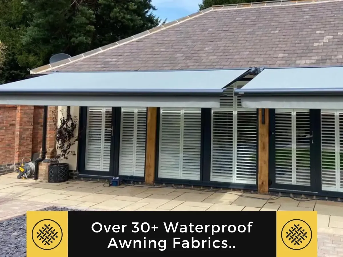 A gray retractable awning installed over glass doors on a house with a tiled roof. A banner reads